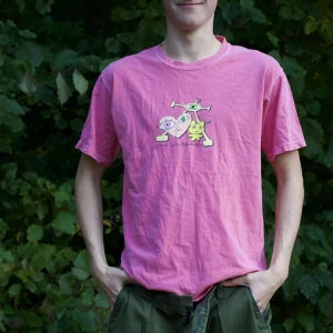 Rosa t-shirt med tryck - Säljer en rosa t-shirt med ett coolt tryck på framsidan. Den är kortärmad och har en normal passform. Perfekt för sommardagar eller avslappnade häng. T-shirten är i bomull och känns skön mot huden. Passar bra till jeans eller shorts!