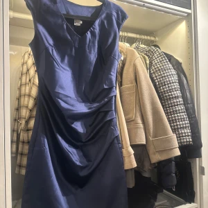 Mörkblå klänning från Saint Tropez - Snygg mörkblå klänning från Saint Tropez i storlek S. Den har en elegant v-ringning och är ärmlös, perfekt för festliga tillfällen. Materialet ser ut att vara satin, vilket ger en lyxig känsla. Passar bra till både höst och vinter.