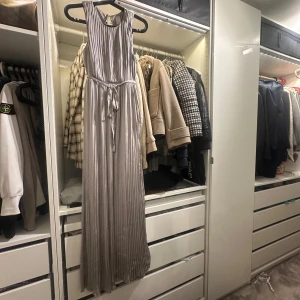 Grå långklänning från Vila - Säljer en elegant grå långklänning från Vila i storlek XS. Klänningen har ett plisserat mönster och är ärmlös med en knytning i midjan för en smickrande passform. Perfekt för festliga tillfällen eller en stilfull kväll.