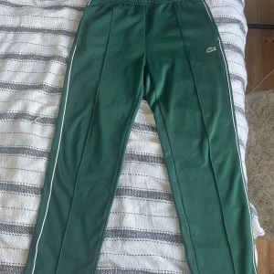 Lacoste Paris pique byxor - Säljer ett par riktigt snygga byxor från Lacoste i regular fit. Byxorna har vita ränder längs sidorna och det klassiska Lacoste-logotypen broderad på framsidan. De är i fantastisk bra skick och redo för en ny ägare!🐊 storleken är xs men väldigt stor i storleken då den passar 180 perfekt