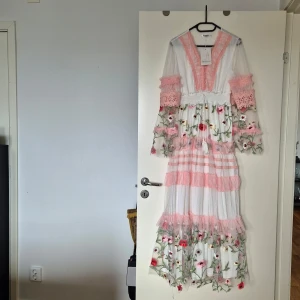 Underbar klänning - stl S,underbart vacker klänning  .Aldrig använd,felköpt . Passar till de flesta tillfällen . Vit med rosa skirt tyg,genomskinligt i armar med vackert blomdekor över klänningen 