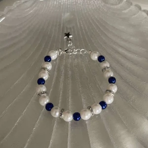 Armband med vita och blå pärlor - Snyggt armband med vita och blå pärlor, perfekt för att piffa upp vilken outfit som helst. Armbandet har en söt stjärnberlock och glittriga detaljer mellan pärlorna. Det är justerbart i storlek och passar de flesta handleder. Perfekt för både vardag och fest! ✨