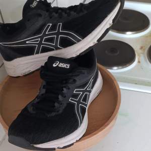 Säljer ett par svarta Asics löparskor i bra skick. De har en snygg vit sula och klassisk Asics-logga på sidan. Perfekta för träning och löpning. Skorna har snörning för en bra passform och är bekväma att ha på sig under längre pass.