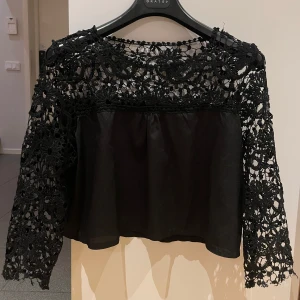 Svart spetsblus - Elegant svart blus med spetsdetaljer och långa ärmar. Perfekt för en stilfull look med en unik design som kombinerar spets och ett slätt tyg. Passar bra till både jeans och kjol.