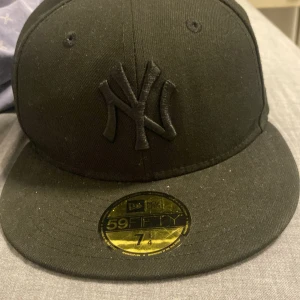 Svart keps från New Era - Snygg svart keps från New Era med broderad logga framtill. Modellen är 59FIFTY och har en klassisk passform. Perfekt för en stilren look.