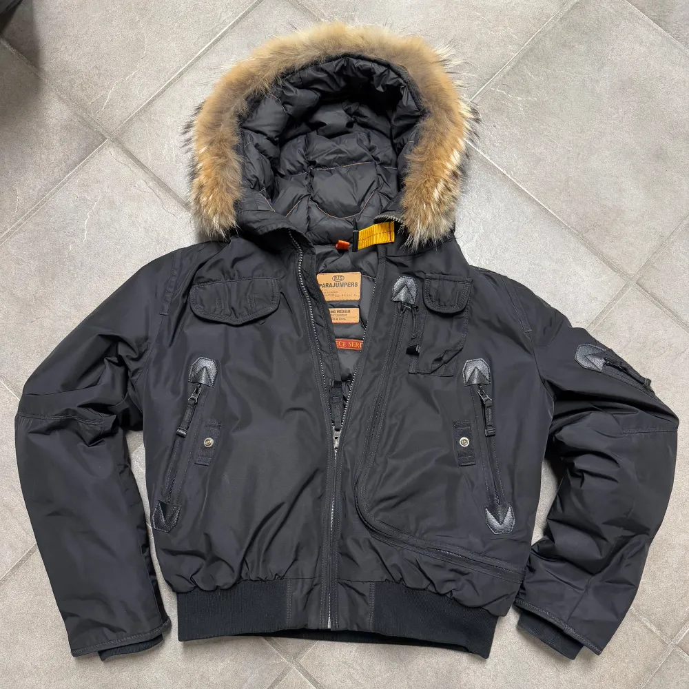Säljer en svart dunjacka från Parajumpers med pälsdetaljer på huvan. Jackan har flera fickor och en dragkedja framtill. Perfekt för kalla dagar med sin varma och skyddande design.. Takit.