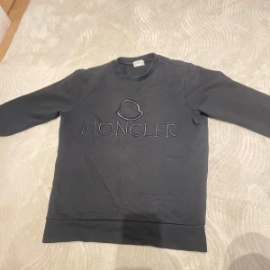 Svart tröja från Moncler - Säljer en stilren svart tröja från Moncler med deras ikoniska logga broderad på framsidan. Tröjan har långa ärmar och en klassisk rund halsringning. Perfekt för en avslappnad och trendig look.