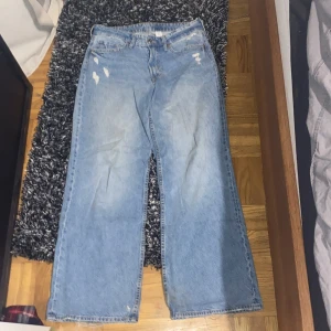 Blå jeansbyxor från H&M - Säljer ett par blå baggy wide, loose fit, mid waist, jeansbyxor från H&M med slitna detaljer. Byxorna har en klassisk femficksdesign och en dragkedja gylf. Dom har används ett par få gånger 