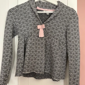 Mönstrad långärmad tröja med rosett - Säljer en snygg mönstrad tröja i svart och vit med en söt rosa rosett framtill. Tröjan har långa ärmar och en bekväm passform. 