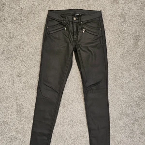 Svarta vaxade  skinny byxor från KappAhl - Snygga svarta skinny byxor från KappAhl med dragkedjedetaljer på fickorna. Väldigt lågmidjade ! Helt nya !