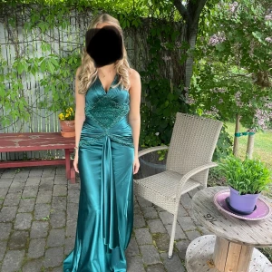 Mörkgrön balklänning med pärldetaljer - Elegant mörkgrön balklänning med v-ringad hals och vackra pärldetaljer vid midjan. Klänningen har en draperad midja och en smickrande passform som ger en glamorös look. Perfekt för speciella tillfälle såsom bal💕endast använd en gång, köpt på plick. Passar både XS OCH S