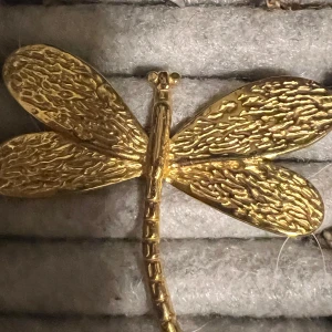 Guldfärgad trollslända ring - Unik guldfärgad ring formad som en trollslända. Den har detaljerade vingar och en justerbar ringdel för att passa olika storlekar. Perfekt för att ge en naturinspirerad touch till din stil.