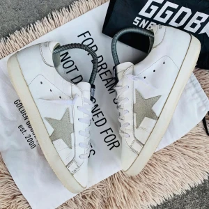 Vita sneakers med stjärndetalj från Golden Goose - Snygga vita sneakers från Golden Goose med en grå stjärndetalj på sidan. Skorna har snörning och en klassisk design med en bekväm sula. Perfekta för en stilren look.