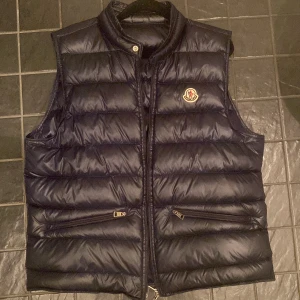 Mörkblå Moncler gui - Säljer en snygg svart dunväst från Moncler. OBS dragkedjan är paj men om någon orkar pilla med det så löser de sig enkelt. Jackan är äkta.