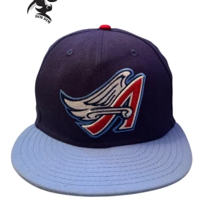 Blå och röd keps med broderad logga - Snygg keps från New Era i mörkblått med ljusblå skärm och röd knapp på toppen. Den har en cool broderad logga framtill med ett vinge-motiv i rött, vitt och blått. Perfekt för att ge din outfit en sportig touch.