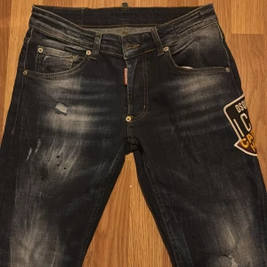 Mörkblå jeans med patch från Dsquared2 - Snygga mörkblå jeans från Dsquared2 med en cool patch på sidan. De har en klassisk femficksdesign och slitna detaljer för en trendig look. Perfekta för dig som vill sticka ut med stil. STORLEK W: 46) L:32