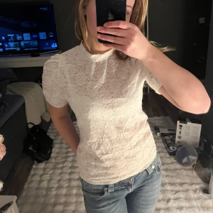Vit spetsblus - Säljer en söt vit spetsblus med korta ärmar. Blusen har ett vackert spetsmönster och en rund halsringning. Perfekt för en stilren och elegant look.