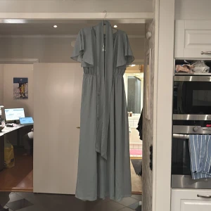 Ljusblå långklänning med volangärmar - Elegant ljusblå långklänning med korta volangärmar och ett flödande fall. Perfekt för speciella tillfällen med sin luftiga design och mjuka material. Klänningen har en markerad midja som ger en smickrande silhuett.