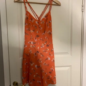 Orange blommig byxdress från BikBok - Säljer en superfin orange typ byxdress från BikBok med blommigt mönster. Den har smala axelband och en kort längd, perfekt för sommardagar. Den är gjord i ett lätt och bekvämt material som känns skönt mot huden. Perfekt för att liva upp garderoben! 🌸