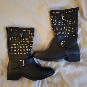 Svarta boots med nitar - Snygga svarta boots med dekorativa nitar och spännen. De har en dragkedja på sidan för enkel på- och avtagning. Perfekta för en edgy look. Står ej storlek på skon men fungerar för mig som är Storlek 39💗
