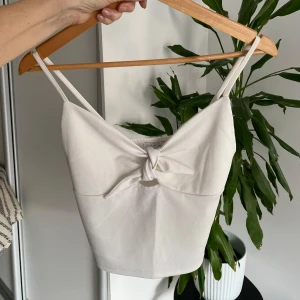 Vit linnetopp med knytdetalj - Säljer en stilren vit linnetopp med smala axelband och en söt knytdetalj framtill. Perfekt för varma sommardagar och kan enkelt matchas med olika outfits.