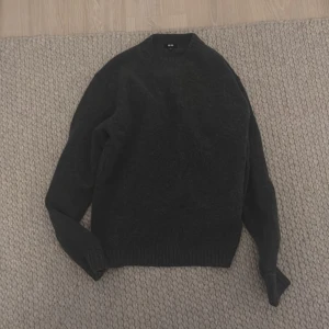 Uniqlo Stickad Tröja Mörkgrå - Säljer en stilren mörkgrå tröja från Uniqlo. Tröjan är långärmad och har en klassisk rund halsringning. Perfekt för kyligare dagar och enkel att matcha med olika outfits.