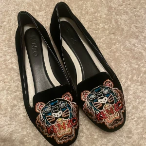 Svarta loafers från Kenzo med broderad tiger - Snygga svarta loafers från Kenzo med en iögonfallande broderad tiger på ovansidan. Skorna har en klassisk design med rundad tå och är tillverkade i ett elegant material.