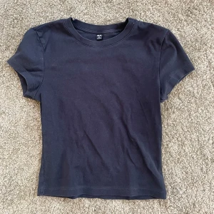 Svart baby tee från Uniqlo - Säljer en klassisk svart t-shirt från Uniqlo i storlek XS. Den har en rund halsringning och korta ärmar, perfekt för en enkel och stilren look. Tillverkad i mjukt material för bekväm passform.