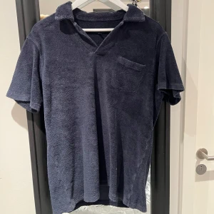 Mörkblå frotté pikétröja från Paul & friends - Säljer en mörkblå pikétröja i frotté med korta ärmar och en bröstficka. Perfekt för en avslappnad stil. Tröjan har en klassisk krage och är skön att bära.