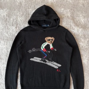 Intressekoll! - Säljer en svart hoodie från Polo Ralph Lauren med en broderad björn som åker skidor på framsidan. Tröjan har långa ärmar och är tillverkad i bomull. Perfekt för en sportig look! Kom med bud!