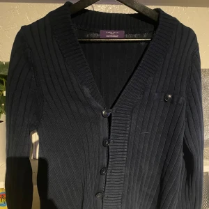 Mörkblå ribbad kofta från Zara Man - Säljer en stilren mörkblå kofta från Zara Man. Den har en ribbad design med knappar framtill och en klassisk krage. Perfekt för att hålla sig varm och snygg under kyligare dagar.