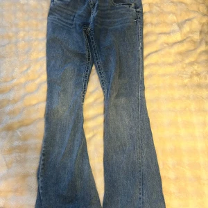 Blå jeans från True Religion - Snygga blå jeans från True Religion med bootcut-stil. Ett par äkta True Religion jeans, som jag vuxit ur. Storlek 29.  Midjemått 75cm. Innerbenslängd ungefär 83 cm. Bakfickan har gått upp lite som man ser på bilden, dock är det inget hål utan bara sömmen som gått upp lite. Annars hela och fina.  Köpte dom för 1600kr och säljer dom för 500kr
