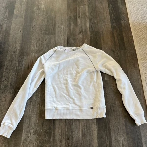 Vit tröja från Tiger of Sweden - Säljer en stilren vit tröja från Tiger of Sweden. Tröjan har långa ärmar och en ribbad nederkant samt ärmslut. Perfekt för en avslappnad och snygg look.