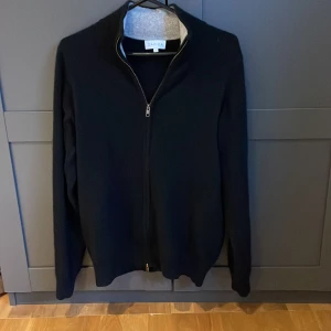 Svart Kashmir full zip - Säljer en stilren svart tröja från Davida med dragkedja framtill. Tröjan har långa ärmar och en enkel design. Perfekt för dig som gillar klassisk stil. 100% Kashmir! Cond 8/10, hör av er vid frågor eller funderingar