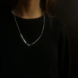 004 - Elegant silverfärgat halsband med en enkel och stilren design. Perfekt för att ge en subtil glans till din outfit. Halsbandet har en tunn kedja med en avlång detalj som ger det en modern touch.