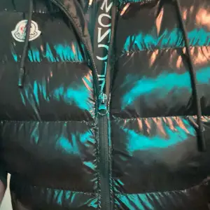 Säljer en snygg svart pufferväst från Moncler. Den är quiltad och har en dragkedja framtill. Jackan är perfekt för vintern och håller dig varm och stilren. Den har en cool Moncler-logga på bröstet och en serietidningsinspirerad etikett på insidan.