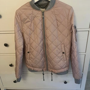 Rosa quiltad bomberjacka från Cream - Säljer en superfin rosa quiltad bomberjacka från Cream. Den har en snygg dragkedja framtill och ribbade muddar i grått vid ärmslut och krage. Jackan har också en cool ficka med dragkedja på ärmen. Perfekt för höst och vår!