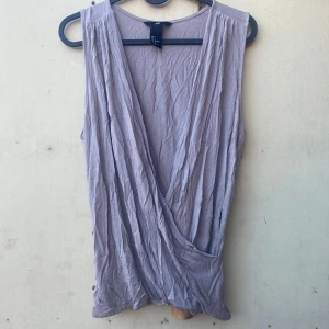 Ljuslila omlottopp från H&M - Säljer en ljuslila omlottopp från H&M. Den är ärmlös och har en snygg omlottdesign framtill. Perfekt för sommardagar eller som ett lager under en kavaj. Toppen är i ett mjukt och bekvämt material.