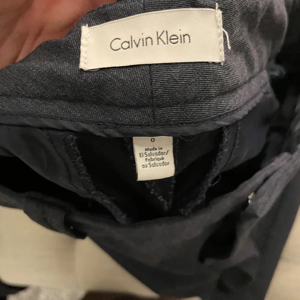 Säljer ett par stilrena grå kostymbyxor från Calvin Klein. De är i ett klassiskt snitt med hällor för bälte och en snygg knappdetalj på bakfickan. Perfekta för både kontoret och finare tillfällen. Bra skick, storlek 0, motsvarar 34. Jeans & Byxor.