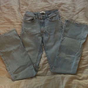 Ljusblå jeans med slitna detaljer - Säljer ett par ljusblå jeans i en avslappnad stil. De har en klassisk femficksdesign och en liten sliten detalj vid fållen som ger dem en cool, vintage look. Perfekta för en casual outfit! De är mid waist