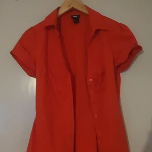 Röd kortärmad skjorta från H&M - Säljer en snygg röd kortärmad skjorta från H&M. Skjortan har en klassisk krage och knappar framtill. . Den är i bra skick och redo för nya äventyr!