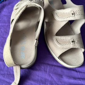 Beige sandaler med kardborreband - Säljer ett par bekväma beige sandaler med kardborreband. De har en robust sula med bra grepp och är perfekta för sommarens äventyr. Sandalerna är i syntetmaterial och har en öppen tådesign.