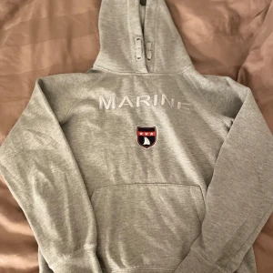 Grå hoodie med MARINE-tryck - Säljer en grå hoodie ifrån Marine tryckt på bröstet under varm och bekväm. Köpt för 500kr 