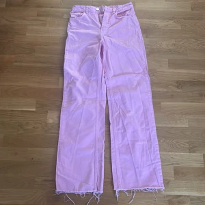 Rosa jeans från Gina Tricot - Säljer ett par snygga rosa jeans från Gina  Jeans i storlek 36. De har en straight passform och är gjorda i ett bekvämt material. Byxorna har en dragkedja och knappar framtill samt fransiga kanter vid bensluten för en cool look. Perfekta för alla