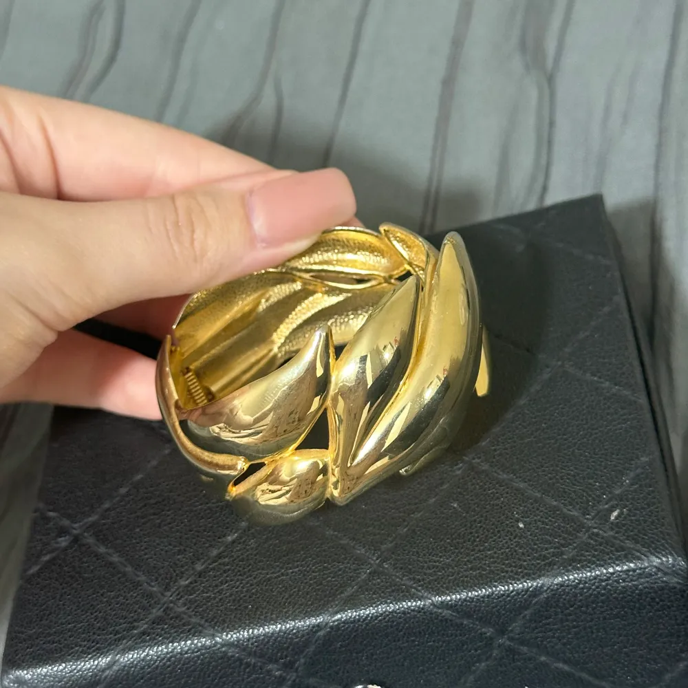 Säljer ett snyggt guldarmband med ett coolt bladmotiv. Armbandet har en unik design med flera överlappande blad som ger en elegant och stilren look. Perfekt för att piffa upp vilken outfit som helst, oavsett om det är till vardags eller fest.💕. Asusteet.
