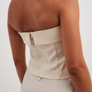 Beige axelbandslös topp - Säljer en superfin beige axelbandslös topp som är perfekt för sommaren. Den har en dragkedja i ryggen och en stilren design som passar både till vardags och fest. 