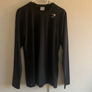 Svart långärmad tröja från Gymshark - Säljer en svart långärmad tröja från Gymshark i storlek S. Perfekt för träning eller vardagsbruk. Tröjan är i nyskick och har en stilren design med Gymshark-loggan på bröstet. Materialet är mjukt och stretchigt för bästa komfort. Passar perfekt för höst och vår!