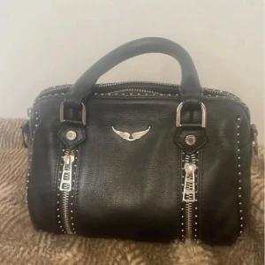 Svart handväska med dragkedja och nitar - Säljer en supercool svart handväska från Zadig! Perfekt för både vardag och fest. Väskan har både handtag och en axelrem Köpte för två år sedan för 5000kr! 😊Litet slitage på handtaget men inget som märks av, enkelt fixat med läderlim om man vill! 💕