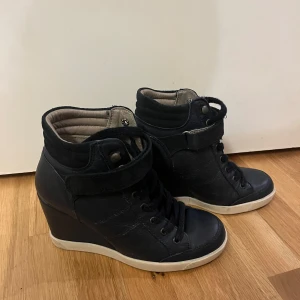 Svarta kilklack sneakers läder från Topshop 37 - Ett par snygga Topshop mörkblå sneakers i läder med kilklack. De har en cool design med snörning och en rem med kardborreband för extra stöd. Skorna är i skinn och har en vit sula som ger en fin kontrast. Perfekta för både vardag & fest! Fint skick