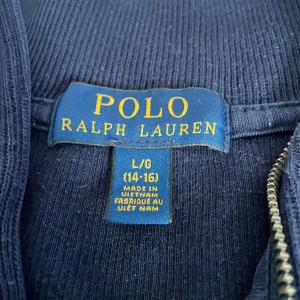 Mörkblå tröja från Polo Ralph Lauren - Säljer en snygg mörkblå tröja från Polo Ralph Lauren. Använd.  Den har en dragkedja vid halsen och det klassiska röda Polo-loggan på bröstet. Perfekt för en stilren och avslappnad look. Rätta storleken kan du se på bilden och inte vid in
